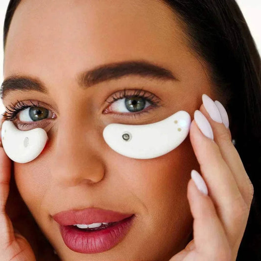 Capsules oculaires blanches en forme de croissant, portées sous les yeux et maintenues délicatement du bout des doigts.
